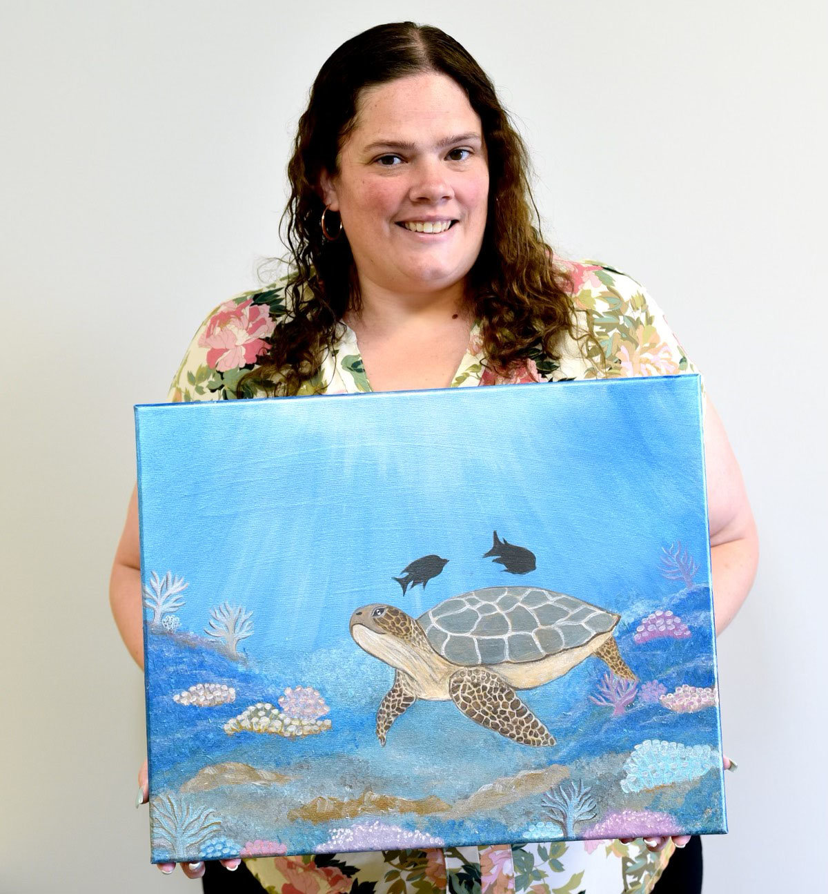 Sarah Torres holds an original sea turtle painting available for bid.